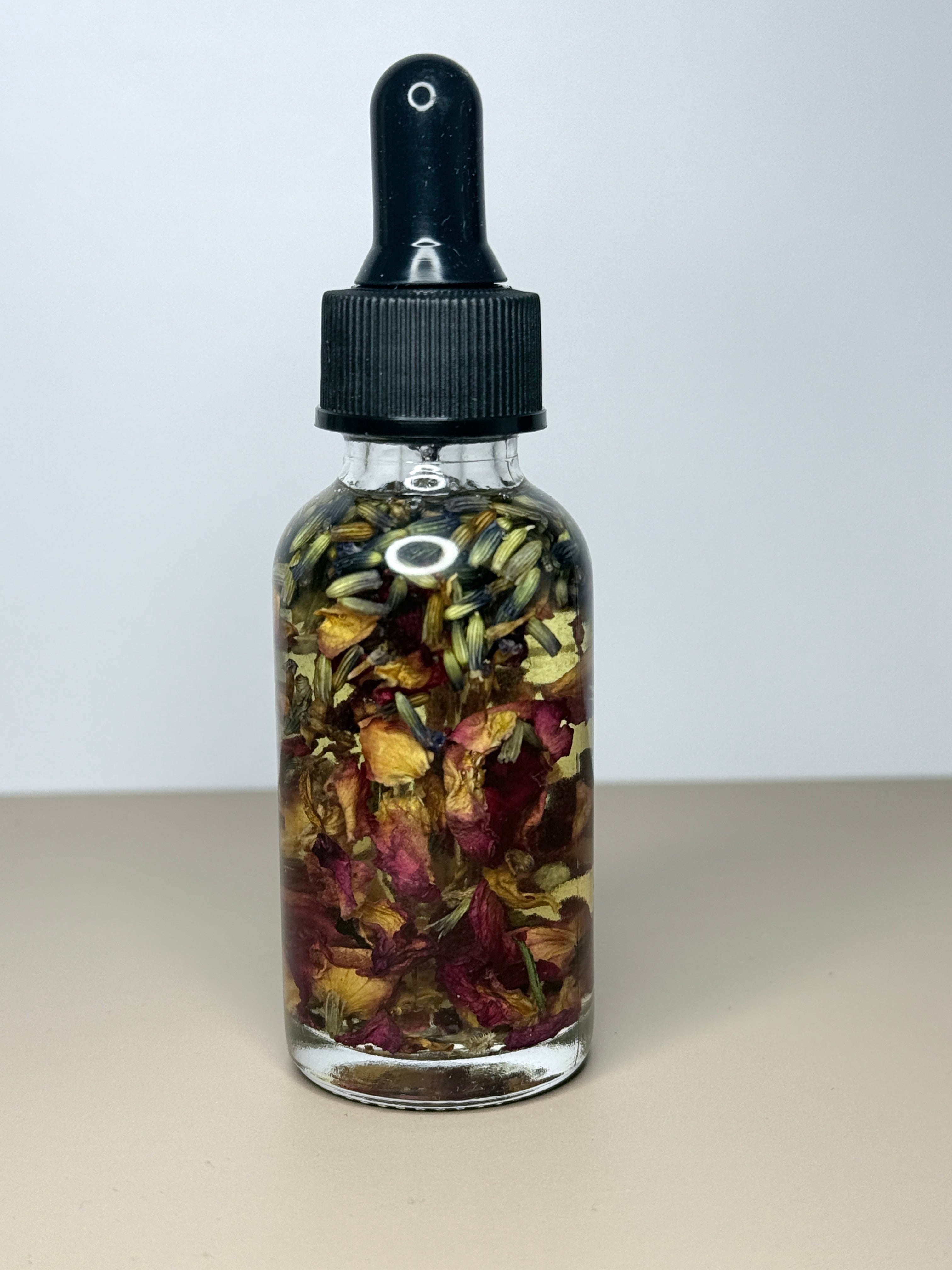 A glass bottle containing a mixture of dried flowers and herbs, with a black dropper cap.