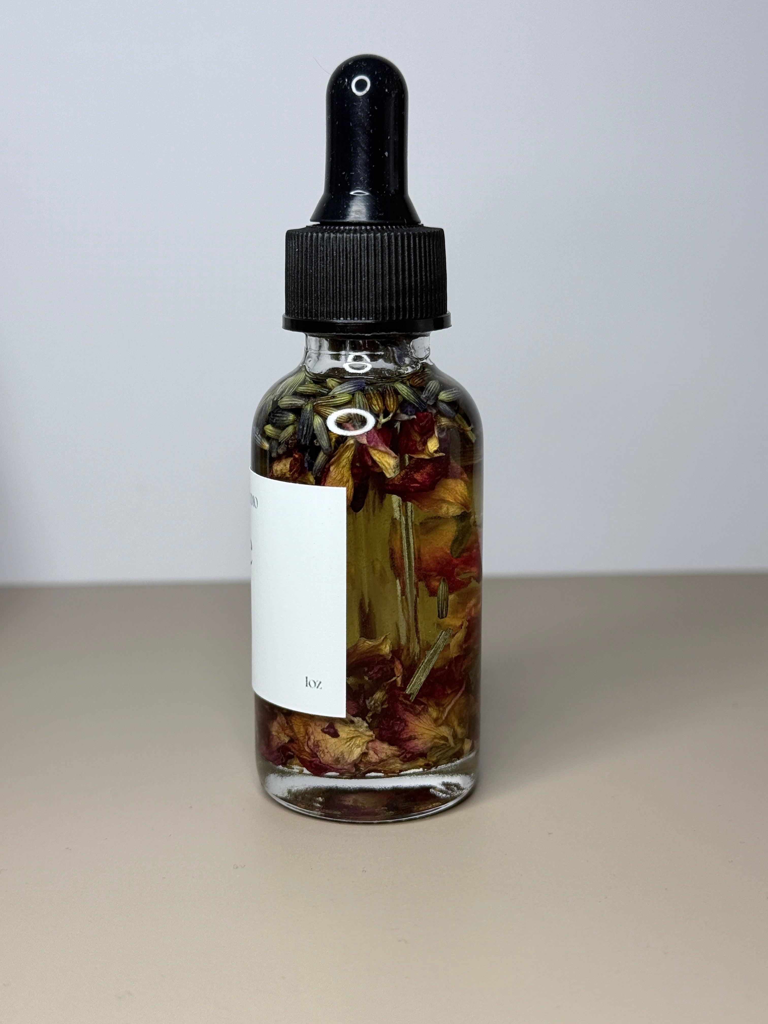 A glass bottle with a black dropper top containing a liquid with dried flower petals floating in it.