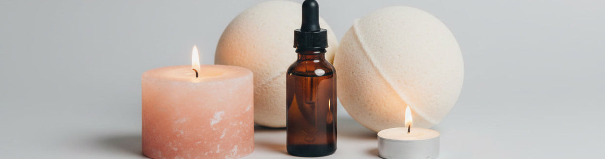 Aromatherapy setup with essential oil dropper, candles, and crystals on a wooden surface.