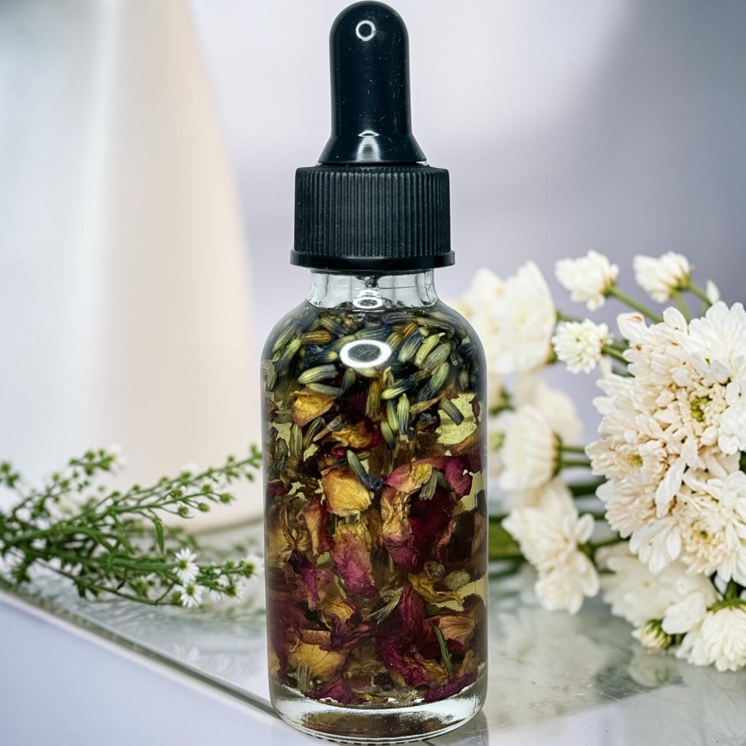 A glass bottle containing a colorful mixture of dried flowers and herbs, placed on a white surface next to a bouquet of white flowers.